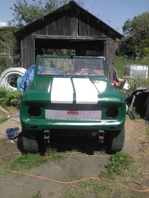 1991 Ford Bronco - A green 1991 Ford Bronco with white racing stripes on the hood is parked in front of a weathered wooden shed. The front of the vehicle show…