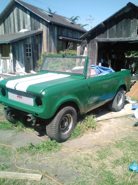 1991 Ford Bronco - A green convertible SUV with white racing stripes on the hood is parked in front of a wooden building. The vehicle appears to be undergoing…