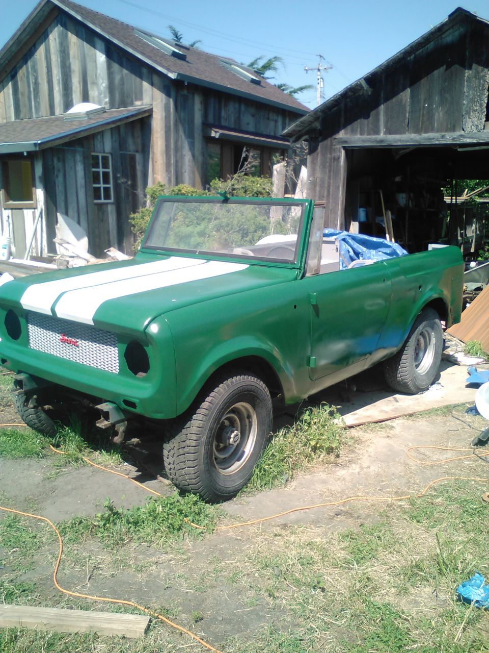 Green convertible SUV with white racing stripes, parked outdoors near a wooden structure.