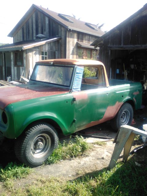 1991 Ford Bronco - A green and red International Harvester Scout pickup truck sits parked in front of a rustic wooden building. The truck is partially restore…