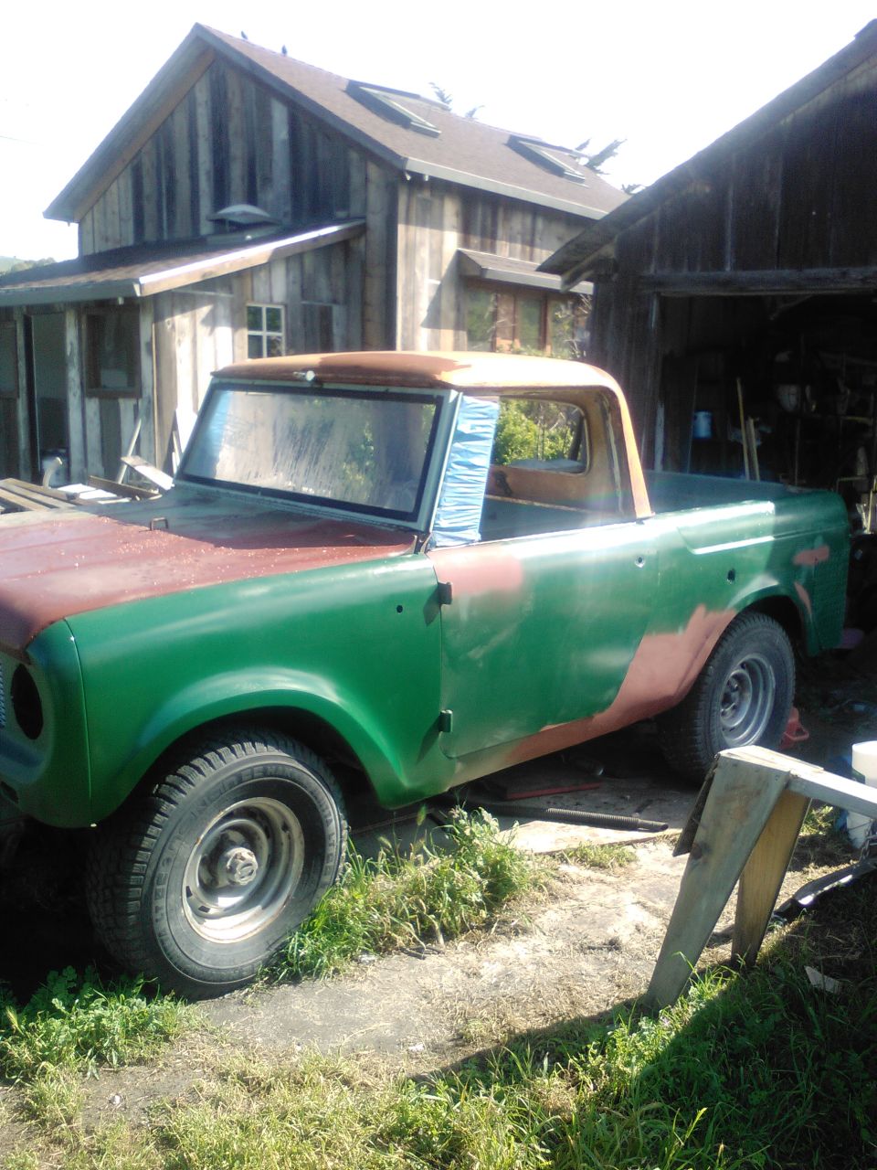 Green and red International Harvester Scout pickup truck with primer patches, parked outdoors.