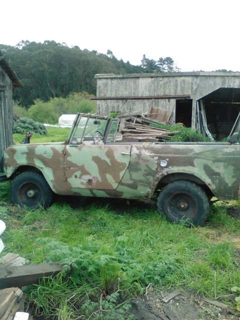 1991 Ford Bronco - A weathered, open-top, four-wheel-drive vehicle with camouflage paint is parked in a grassy area next to a rustic wooden structure. The veh…