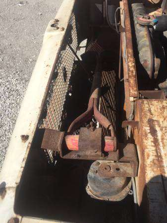 1991 Ford Bronco - A close-up, high-angle shot shows the rusty, industrial components of a vehicle's undercarriage. Visible are metal grating, a red and orang…