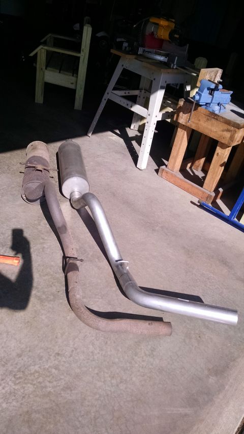 1994 Ford Bronco - Two exhaust systems are laid out on a concrete surface. One is a rusted, older system with a muffler, and the other is a newer, shiny syste…