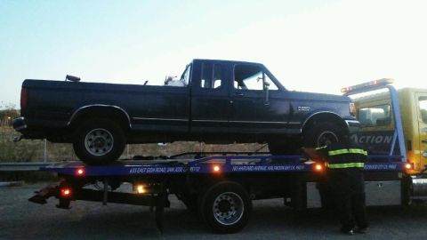1991 Ford Bronco - A dark blue Ford pickup truck is loaded onto a yellow tow truck. The tow truck has text that reads "ACTION" and lists addresses in San Jose…