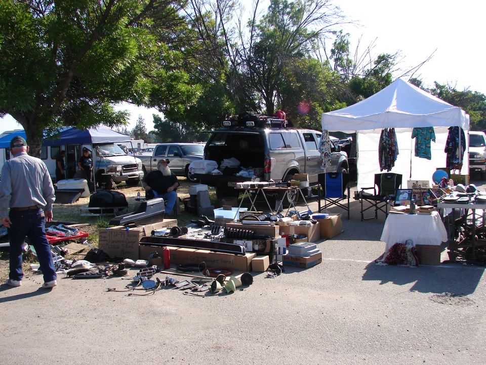 Vehicle parts displayed at an outdoor sale, with a canopy tent and parked vehicles in the background.
