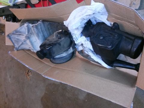 1996 Ford Bronco - Two automotive parts, likely power steering components, are placed inside a cardboard box. One part is silver and black, while the other is…