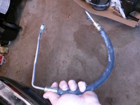 1996 Ford Bronco - A person's hand holds a flexible hydraulic hose with metal fittings on both ends. The hose is dark gray and curved into a U-shape, with one…