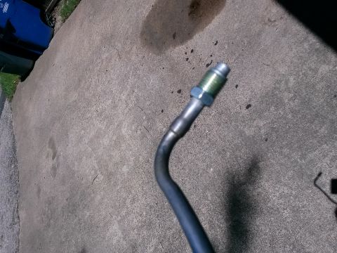 1996 Ford Bronco - A close-up view of a metal brake line with a green fluid fitting attached, resting on a concrete surface.