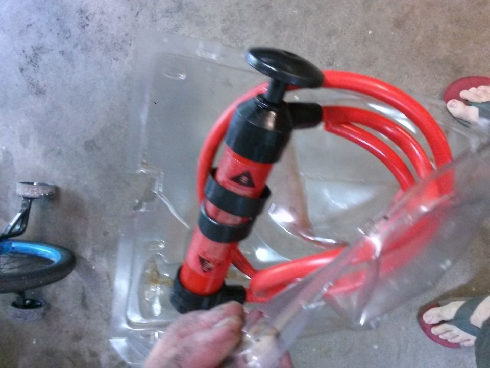Red and black bicycle pump in packaging with a bicycle wheel nearby.