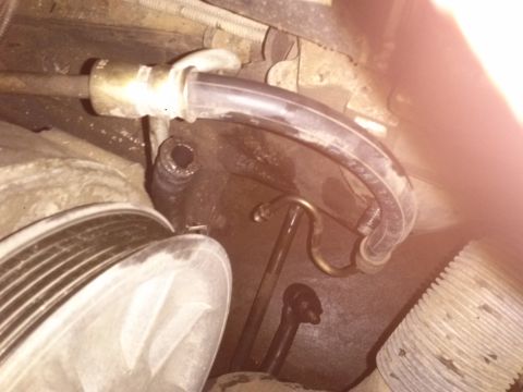 1996 Ford Bronco - A close-up view of engine components, including a ribbed pulley and various hoses and metal lines. A clear plastic hose with text visible i…