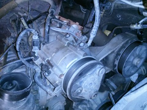1996 Ford Bronco - A close-up, overhead view of the engine bay of a 1996 Ford Bronco, focusing on the air intake system and the air conditioning compressor.