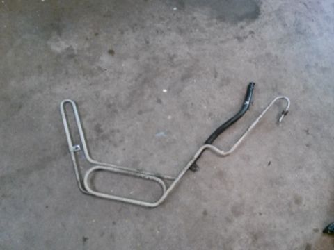 1996 Ford Bronco - A bent metal tube with a black rubber hose attached to one end lies on a concrete surface. The metal tube is silver and has several bends a…