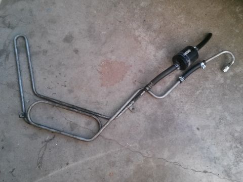 1996 Ford Bronco - A metal fuel line assembly with a black filter is laid out on a concrete surface.