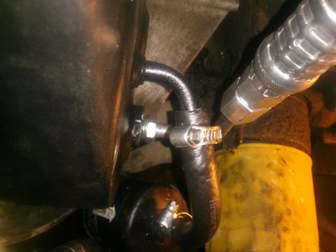 1996 Ford Bronco - A close-up view shows a black hose with a metal clamp attached to a fitting on a black reservoir. A silver hydraulic line connects to the f…