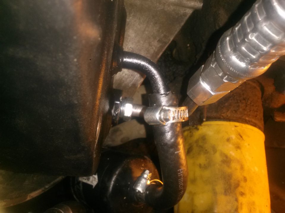 Hydraulic line connected to reservoir fitting with hose clamp and oil filter.