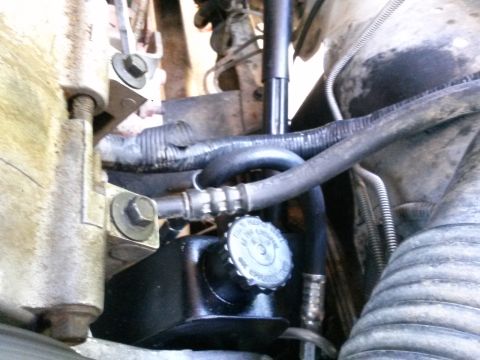 1996 Ford Bronco - Close-up view of the power steering pump reservoir and hoses in a vehicle engine bay. A metal bracket with a bolt is visible to the left of…