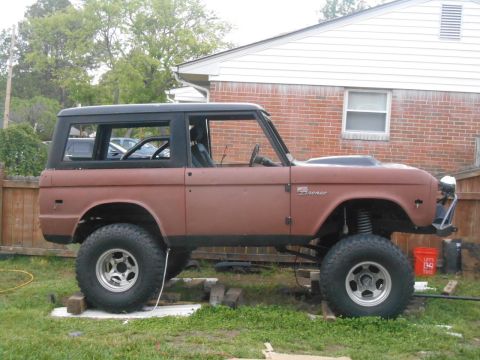 1972 Ford Bronco - A lifted 1972 Ford Bronco is parked on blocks in a grassy yard next to a brick house. The vehicle has a brown body, black top, and large of…
