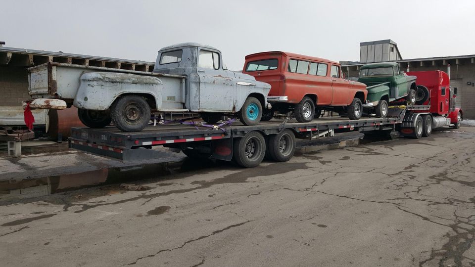Three vintage trucks on a flatbed trailer towed by a red semi-truck.