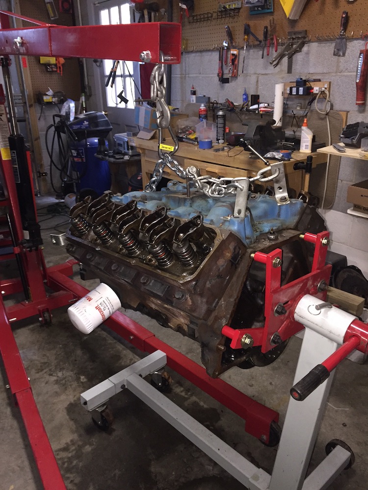 V8 engine block on stand with engine hoist and oil filter.