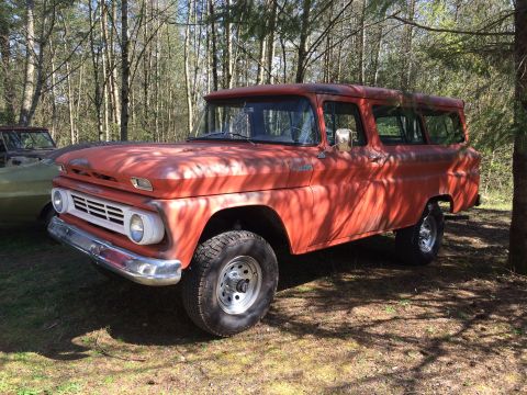 1962 Chevrolet Suburban - A vintage orange Chevrolet Suburban is parked outdoors in a wooded area. The vehicle has a white grille and chrome bumper, and appears to b…