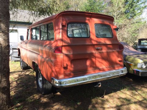 1962 Chevrolet Suburban - The rear passenger side of a vintage orange Chevrolet Suburban is parked outdoors next to a house and another vehicle covered with a tarp.…