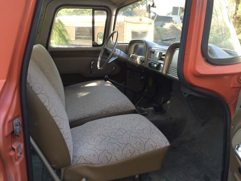 1962 Chevrolet Suburban - The interior of an orange classic truck is shown, featuring tan and patterned fabric seats, a dashboard with a radio, and a steering wheel.…