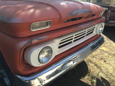 1962 Chevrolet Suburban - Close-up front view of a vintage orange pickup truck with a chrome bumper and white grille. The truck has a weathered paint job and visible…