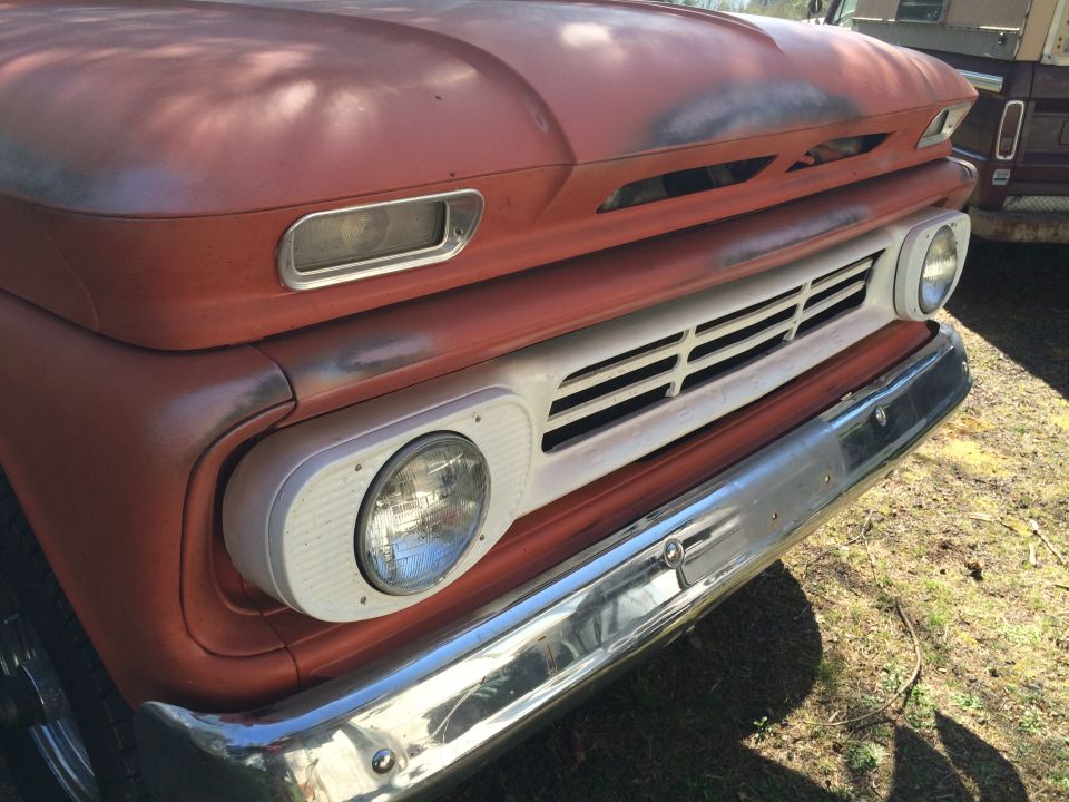 Weathered orange vintage pickup truck front view with chrome bumper and white grille.