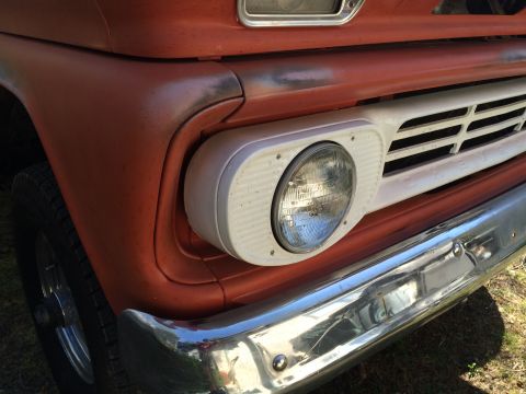 1962 Chevrolet Suburban - Close-up of the front passenger side of an orange Chevrolet truck, showing the headlight assembly, grille, and chrome bumper. The vehicle a…