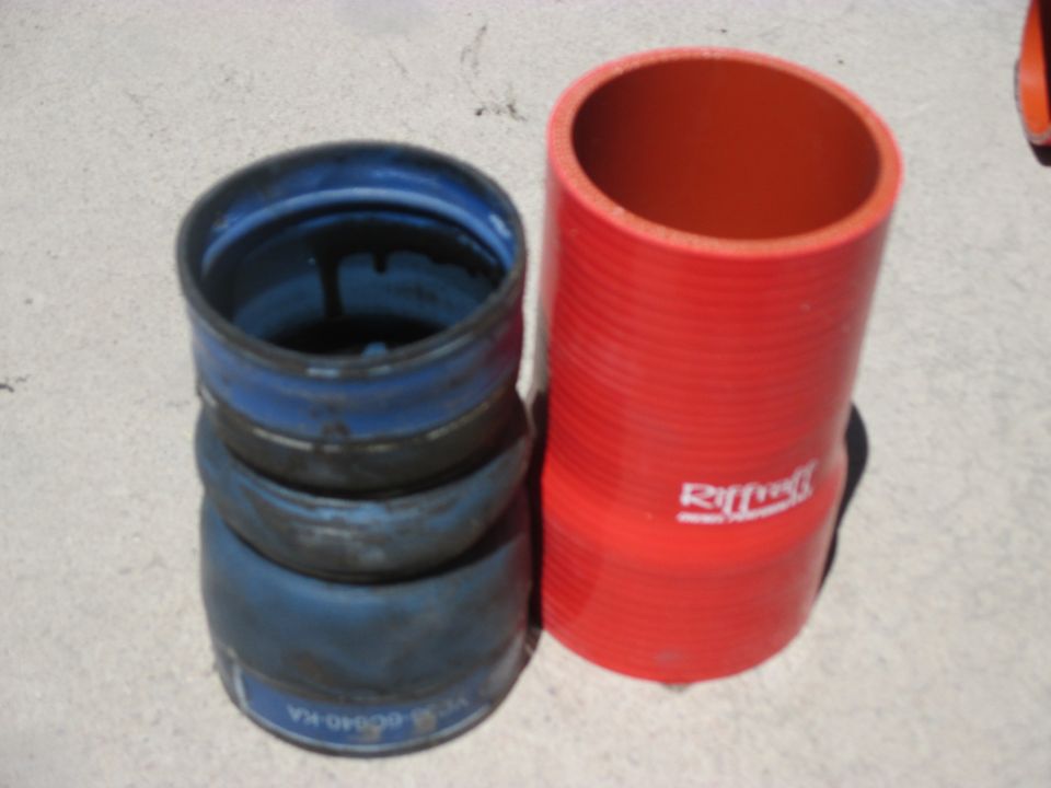 Old blue rubber hose coupler next to new red silicone coupler on concrete