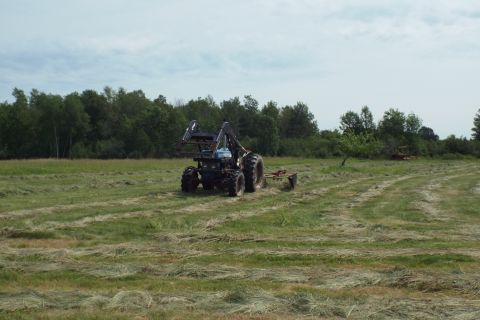 1963 Hummer H3 - A tractor equipped with a loader and mower operates in a freshly cut field, with another piece of farm equipment visible in the background.