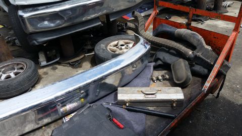 1992 Ford Bronco - Various automotive parts, including a chrome bumper and air intake components, are organized on a utility cart.