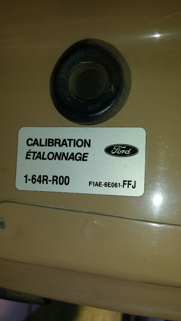 Tan panel with a black rubber grommet above a white Ford calibration sticker