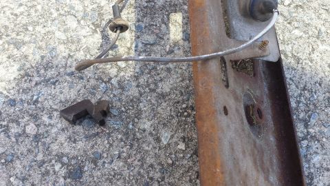1976 Ford Ranchero - A close-up view of a rusty metal bracket with a detached clip and wire, resting on a concrete surface.
