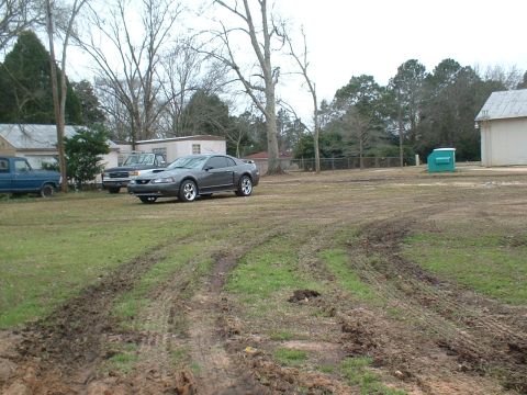 2003 Ford Mustang - A gray 2003 Ford Mustang coupe is parked in a grassy area with muddy tire tracks visible.