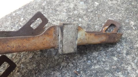 1976 Ford Ranchero - A close-up view of a corroded metal bracket with a block attached, resting on a textured surface.