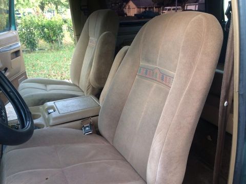 1990 Ford Bronco - The interior of the vehicle shows tan cloth seats with a patterned stripe and a center console with cup holders.