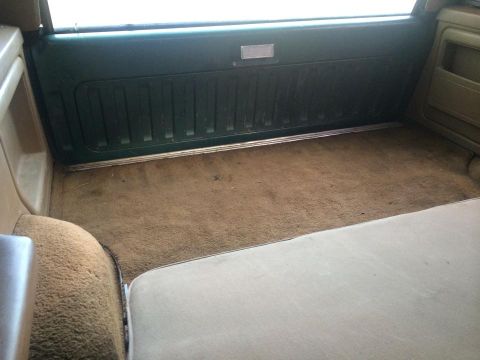 1990 Ford Bronco - The cargo area of the vehicle shows worn brown carpeting and dark green interior paneling.