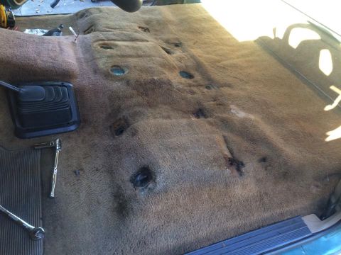 1990 Ford Bronco - The interior floor of a vehicle is shown with the carpet removed, revealing the underlying structure and a gear shifter boot.