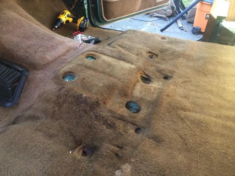 1990 Ford Bronco - Interior floor of a vehicle with carpet removed, revealing mounting points and tools for repair.
