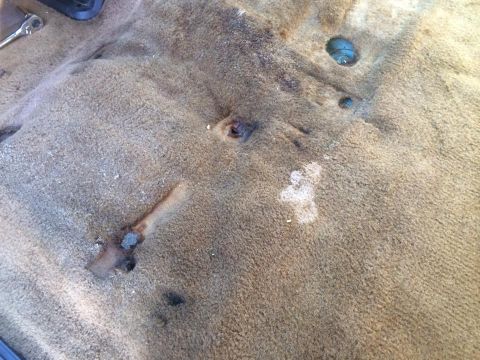 1990 Ford Bronco - Close-up of worn vehicle interior carpet with visible rust and damage.