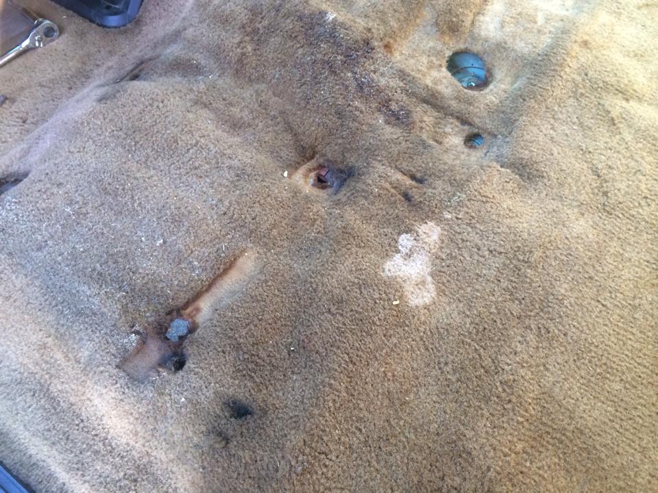 Interior carpet of a vehicle showing wear, rust spots, and damage