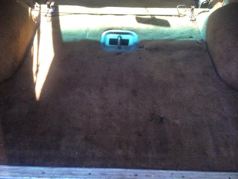 1990 Ford Bronco - The cargo area of a vehicle shows brown carpeting and a blue latch mechanism.