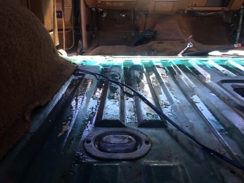 1990 Ford Bronco - The interior of a vehicle shows a wet, green metal floor after carpet removal, with wiring visible.