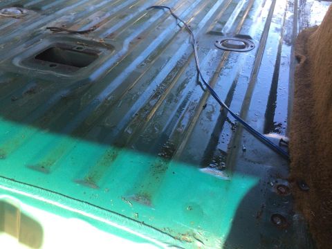 1990 Ford Bronco - The interior cargo area of a vehicle shows a ribbed floor with a blue wire running across it and a carpeted section on the right.