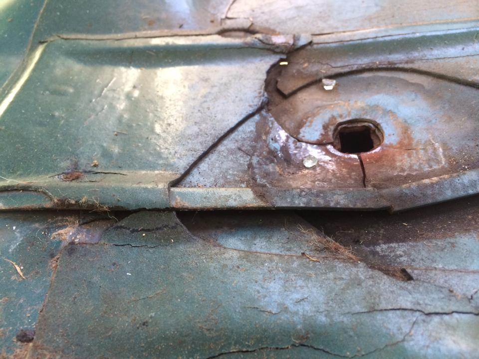 Close-up of a corroded metal panel with a square hole and some debris