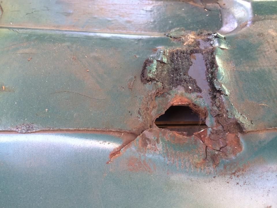 Green vehicle panel with large rust hole and peeling paint
