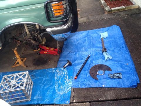 1990 Ford Bronco - Front wheel assembly of a 1990 Ford Bronco is disassembled, with parts laid out on blue tarps.