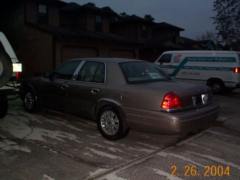 2003 Ford Crown Victoria - A 2003 Ford Crown Victoria is parked next to a white van.